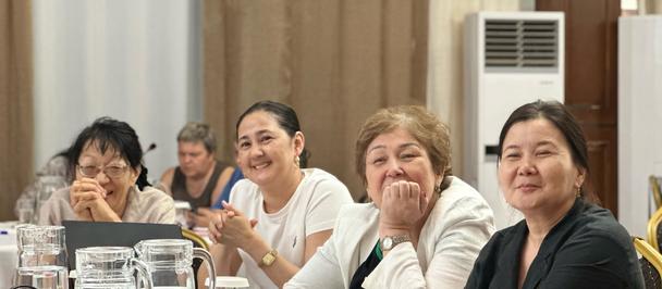 Five women seated at a white-tablecloth dining table, smiling with drinks.