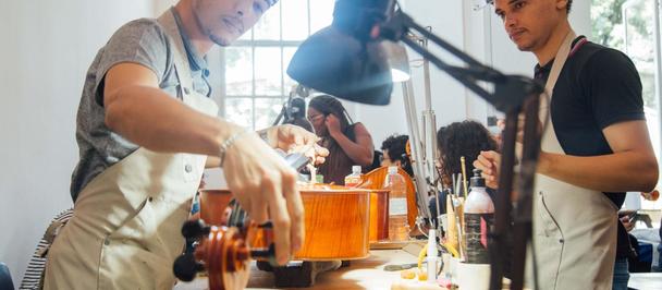 Photo: group of people in a bright workshop crafting orange wooden pieces at a workbench.