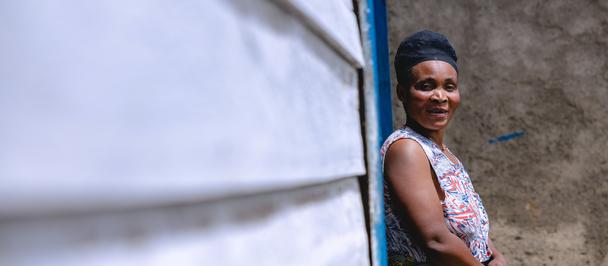 Photograph of a smiling woman in a patterned dress standing beside a blue wall.