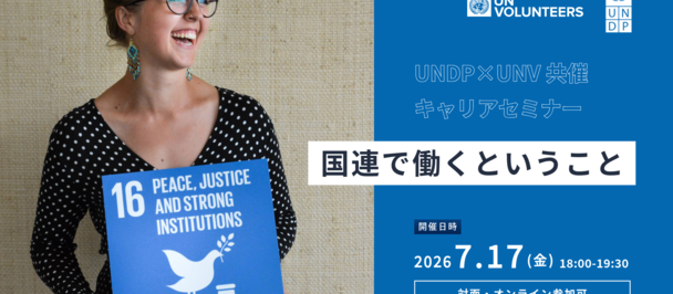 Photo of a woman with glasses holding a blue placard marked 16 beside a UN Volunteers banner.