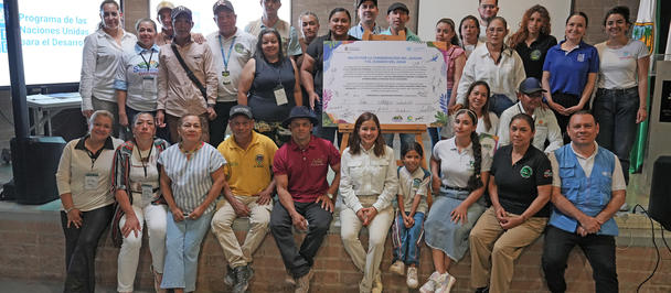 Diverse group posing indoors for a workshop photo, holding a large banner.