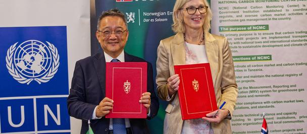 Two professionals in suits hold red folders at a signing ceremony, UNDP banner in background.