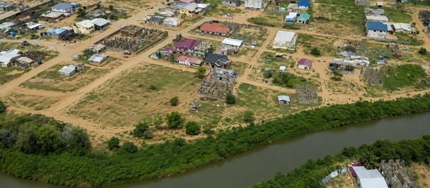 Aerial view of a rural town along a winding river with houses and dirt roads.