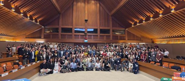 Large group portrait in a timber-paneled hall with a vaulted ceiling and warm lighting.