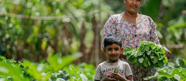 Photograph: mother and child in a lush garden, smiling among leafy greens.