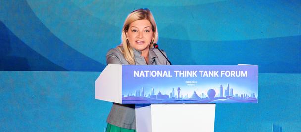 Female speaker at podium on blue backdrop for National Think Tank Forum.
