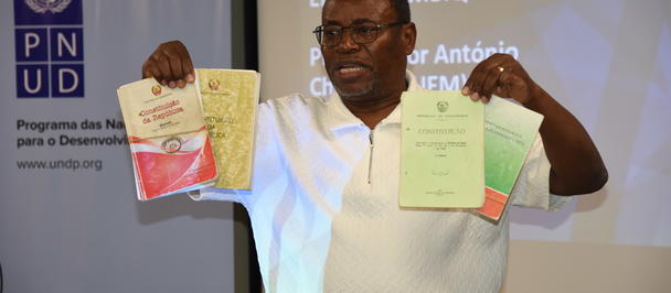 Photo of a man in a white shirt holding two documents beside a UNDP banner and a projector screen.