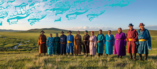 Group photo of people in colorful robes standing in a grassy field with distant hills.