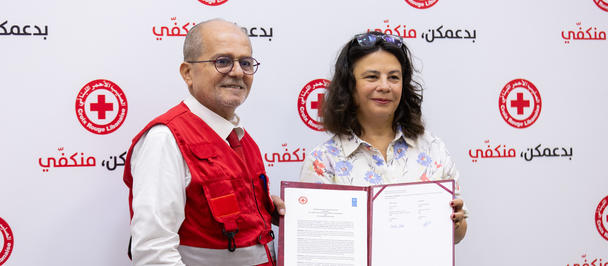 Two smiling people in front of a red cross backdrop; the woman holds an open certificate.