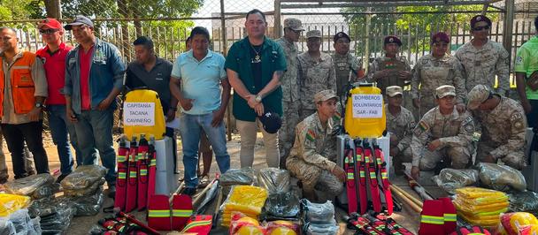 Group of soldiers and civilians pose with aid supplies on an outdoor court.