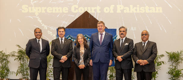 Group of men in suits posing on stage; banner behind reads Supreme Court of Pakistan.