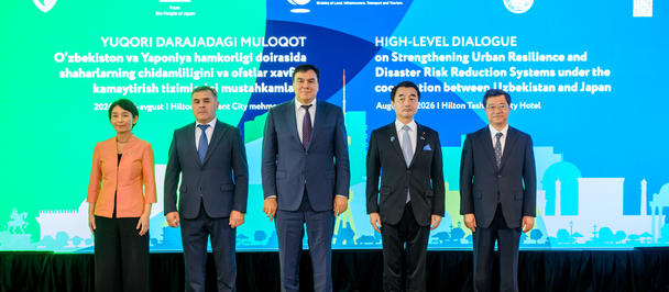 Six people in formal attire stand on a stage in front of a blue backdrop with logos.