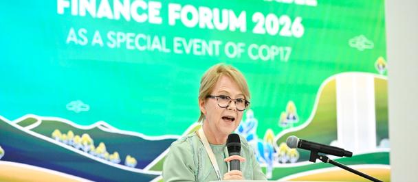 Female speaker at podium during High-Level Sustainable Finance Forum 2026, UN banner behind.