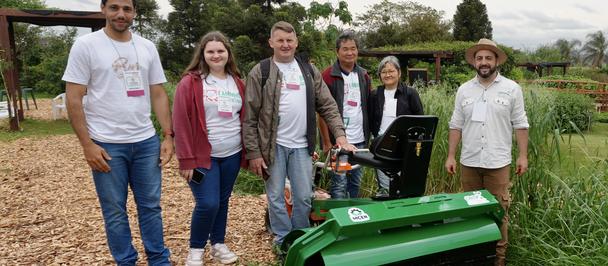 Group posing outdoors beside a green robotic lawn mower.