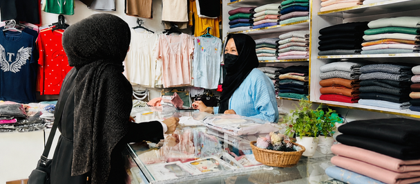 Boutique store with stacked folded clothes, hanging shirts, and customers at a glass counter.