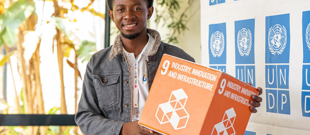Smiling young man in a denim jacket holds orange sign with recycling icons in front of UN logos backdrop.