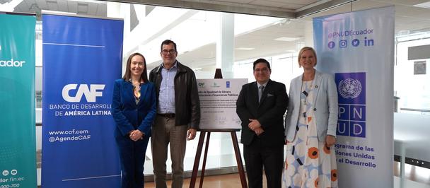 Group of people posing with a framed plaque in a conference room, flanked by blue banners.