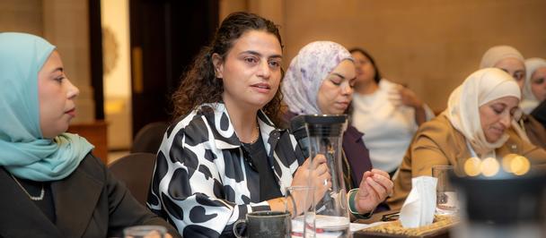 Photograph of women around a conference table; central woman in a black-and-white blouse.