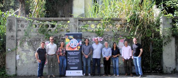 Group of people posing on a sidewalk in front of a stone wall with a banner.