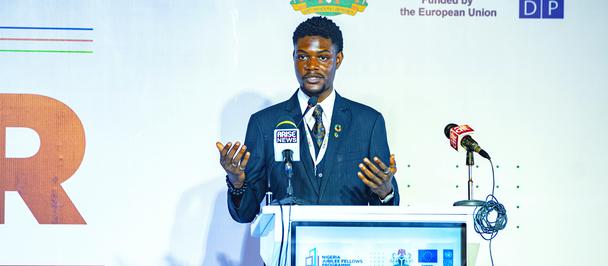 Photograph of a man in a suit giving a speech at a job fair stage with UNDP banners.
