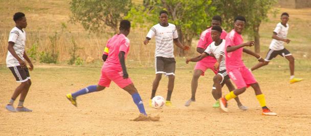 Photograph of young players on a dusty field playing soccer in pink and white kits.