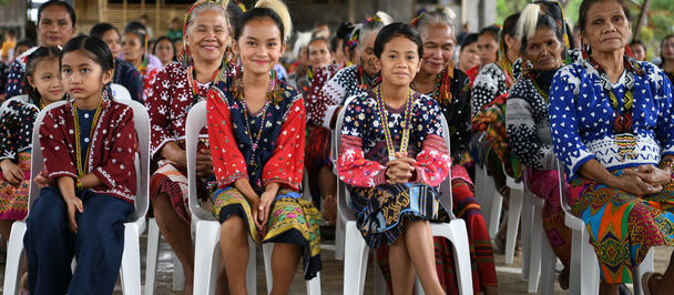 Group of people in colorful traditional outfits sitting in a row outdoors.
