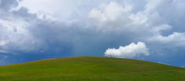Photo of a green hill under a dramatic cloudy sky.