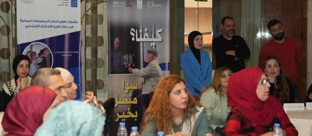 Group of women in hijabs seated around a long table with plates and drinks at a community event.