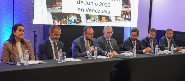 Panel of speakers seated at a long table on stage; projection screen behind shows a PDNA banner.
