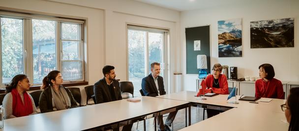 Photo of people in a meeting around a long conference table in a sunlit room with wall art.