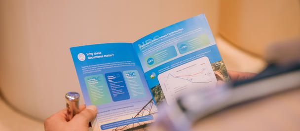 Close-up of a hand with rings holding a blue brochure with charts and diagrams.