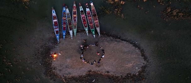 Campfire circle in a forest clearing at dusk, with a small fire and colorful banners around.