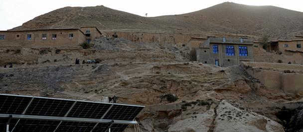 Desert hillside with adobe houses, a blue building, and solar panels in the foreground.