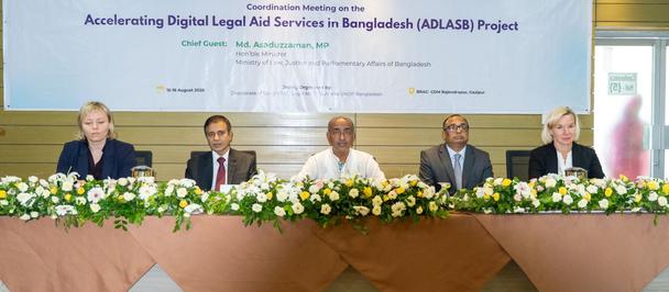 Photograph: five panelists seated at a long table with flower arrangements, banner behind them.
