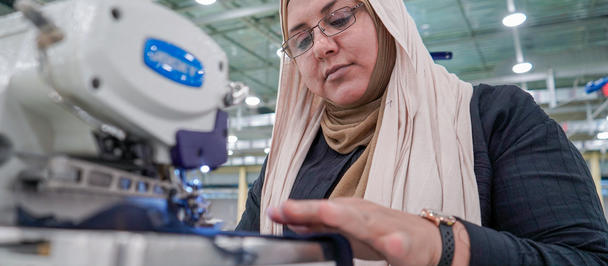 Focused woman in hijab operating an industrial sewing machine in a workshop.