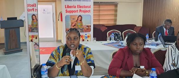 Two women sit at a table with microphones during a conference; banners in the background.
