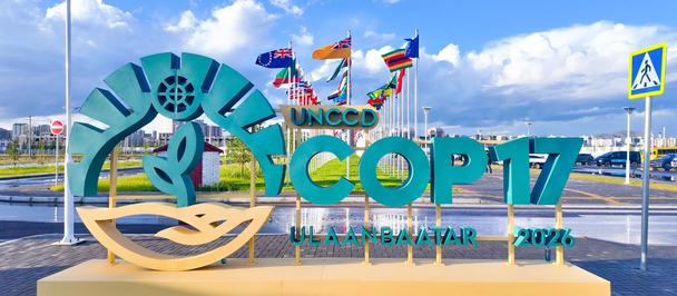 Colorful seaside sign sculpture with a wheel logo and teal letters on a yellow pedestal, against blue sky.