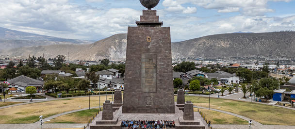 Stone monument with a globe atop a tall pedestal in a circular plaza, with distant hills.