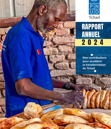 Man in a blue shirt preparing bread with a brick wall in the background.