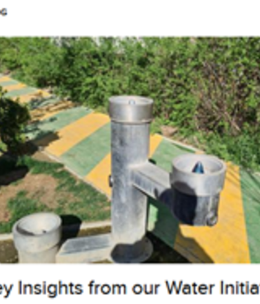 Metal water fountain in a green park with a yellow and green pathway.
