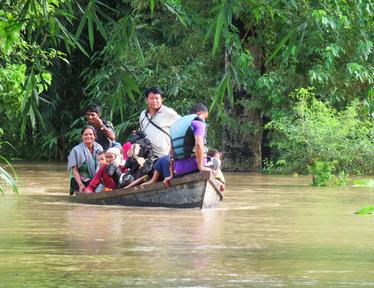 A group of people in a boat navigating floodwaters surrounded by lush green vegetation.