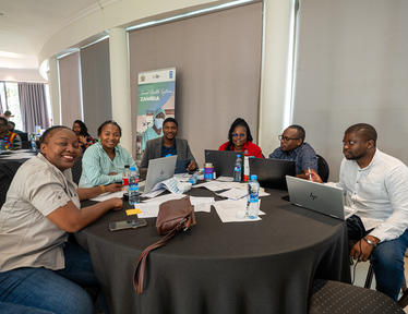 Diverse group of professionals gathered around a round table in a workshop, smiling.