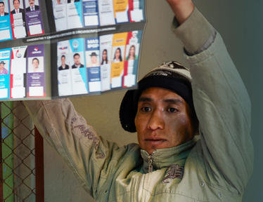 Person with arms raised beside a display board of portrait photos near a fence.
