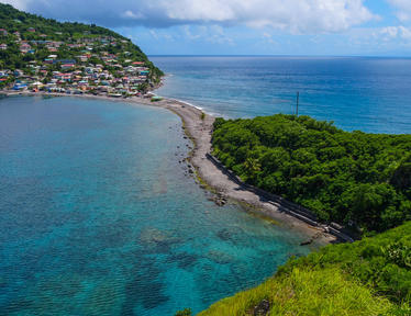 Photograph of a turquoise coastal inlet with a rocky jetty and green cliffs.