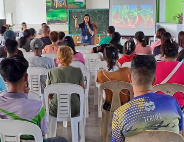 Photo: classroom workshop with a speaker at the front, audience seated, slides on screen.