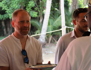 Photo of an outdoor picnic; foreground person in a white shirt with sunglasses on chest.