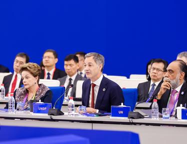 Group photo of officials seated at a conference table on a blue stage.