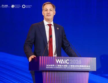 Photograph of a man in a dark suit and red tie speaking at a WAIC podium on a blue stage.