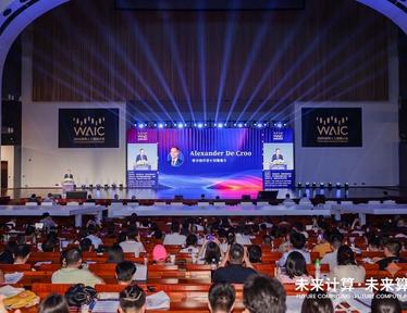 Large conference hall filled with audience watching a stage with blue lighting and screens.