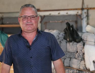 Middle-aged man with glasses in a blue patterned shirt standing in a rustic barn.